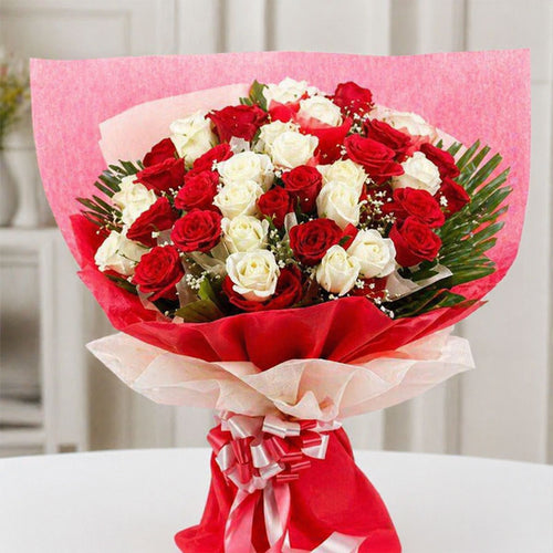 Bouquet of red and white roses wrapped in pink paper on a white surface.