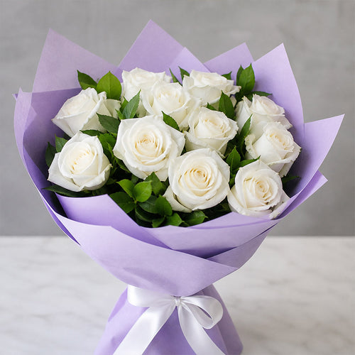 Bouquet of white roses wrapped in purple paper with a white ribbon on a gray background