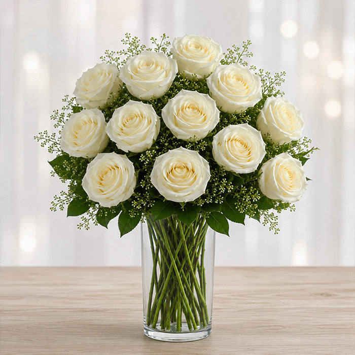Bouquet of white roses in a clear vase on a wooden surface with a blurred light background