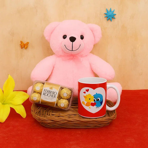 Pink teddy bear, Ferrero Rocher chocolates, and a mug with a heart design on a wooden surface.