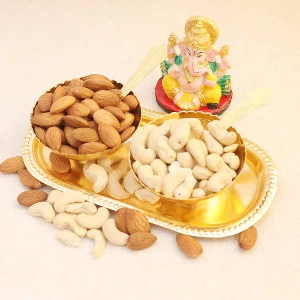 Almonds and cashews on a gold tray with a small idol on a white background
