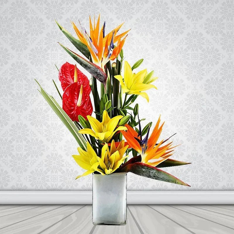 Colorful floral arrangement with red, yellow, and orange flowers in a white vase on a light gray background.