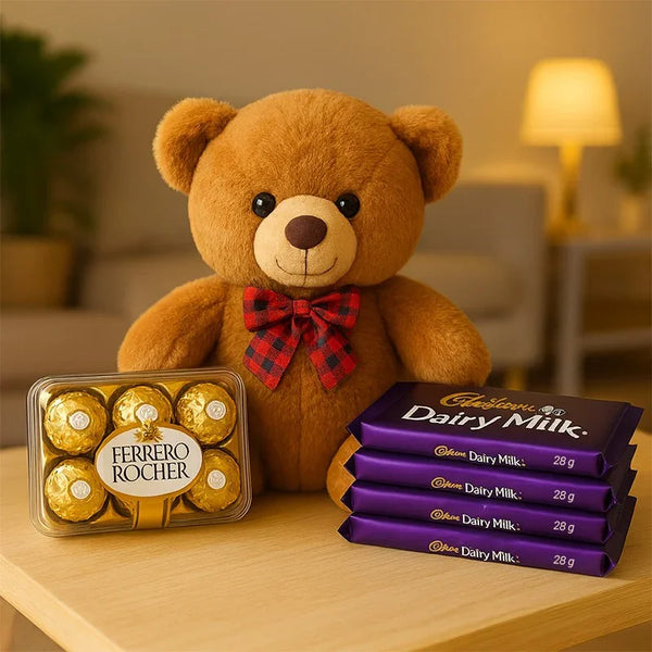 Brown teddy bear with red bow, Ferrero Rocher chocolates, and Dairy Milk bars on a table.