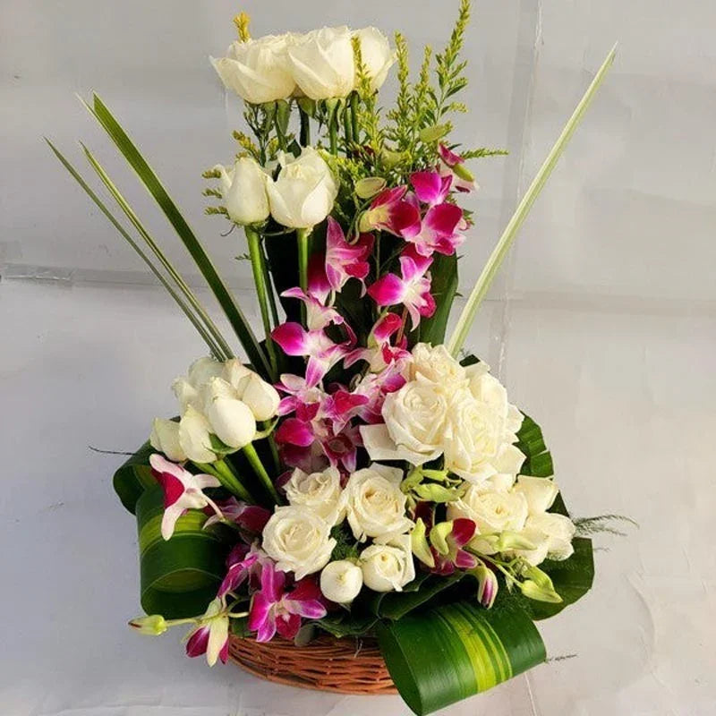 Bouquet of white roses and pink orchids in a woven basket against a plain background