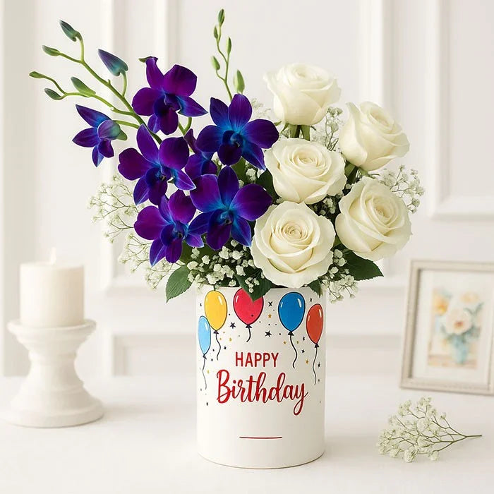 Bouquet of white roses and purple orchids in a 'Happy Birthday' decorated vase on a white surface.