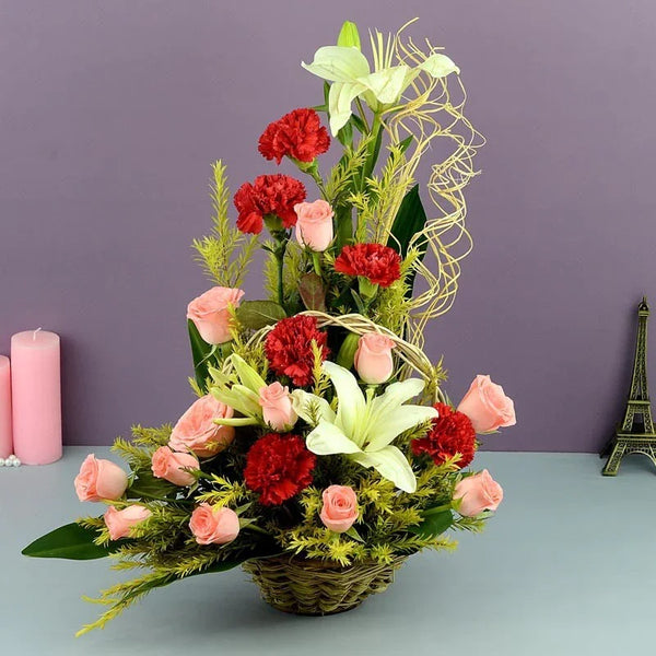 Floral arrangement with red and pink flowers in a basket on a gray surface with a purple wall background.