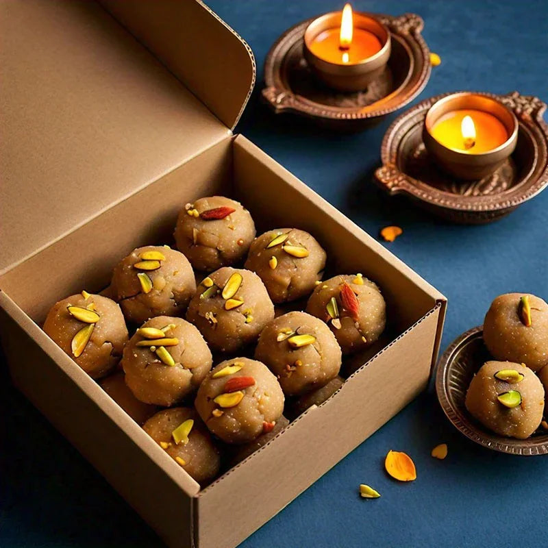 Box of besan ladoo garnished with nuts, surrounded by lit diyas on a festive table