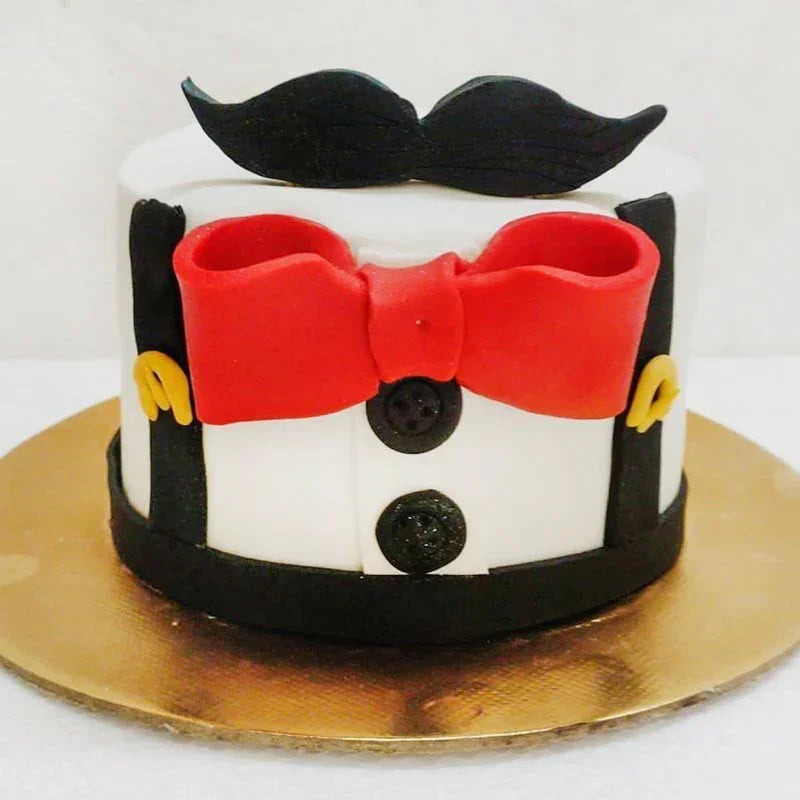 Cake decorated like a character with a red bow tie, black mustache, and buttons on a white background.