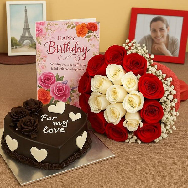 Heart-shaped chocolate birthday cake, red and white rose bouquet, and birthday card on table