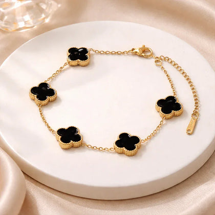 Gold bracelet with black clover-shaped charms on a white plate