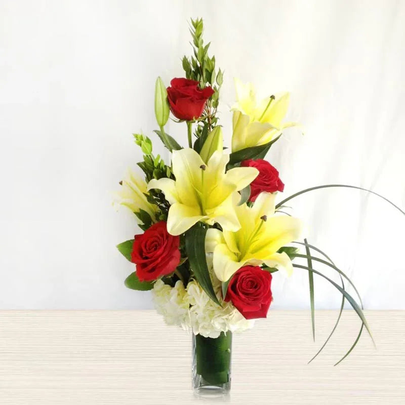 Bouquet of red roses and yellow lilies in a clear vase on a white background