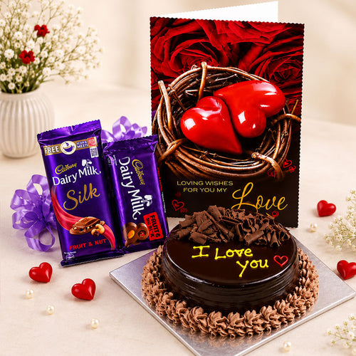 Chocolate cake with 'I Love You' text, Cadbury Dairy Milk Silk chocolate bars, and a card with red hearts on a decorative background.
