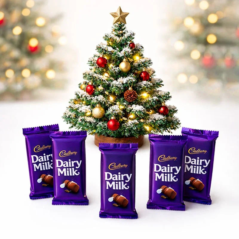 Cadbury Dairy Milk chocolate bars in front of a decorated Christmas tree with blurred lights in the background.