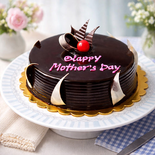 Chocolate cake with 'Happy Mother's Day' on a white plate with flowers in the background