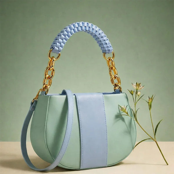 Light blue and green handbag with braided handle on a beige surface with a green background