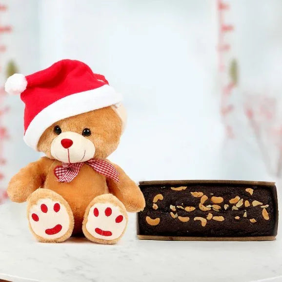 Cute teddy bear in Santa hat with chocolate nut cake on white table, holiday gift combo