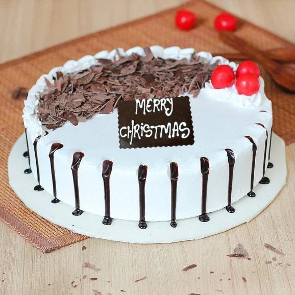 Christmas chocolate cake with whipped cream, chocolate shavings, cherries, and a 'Merry Christmas' tag.