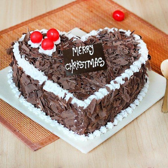 Heart-shaped chocolate cake with white cream, red cherries, and 'Merry Christmas' sign