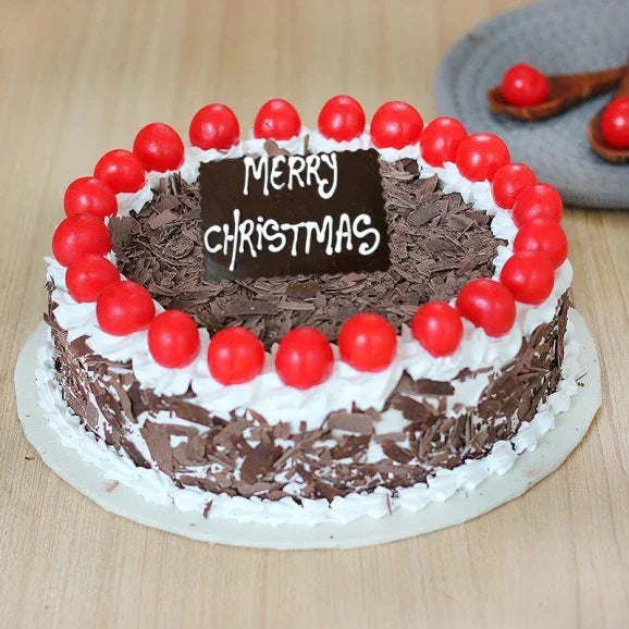 Chocolate Christmas cake with red cherries, whipped cream, and Merry Christmas message on top
