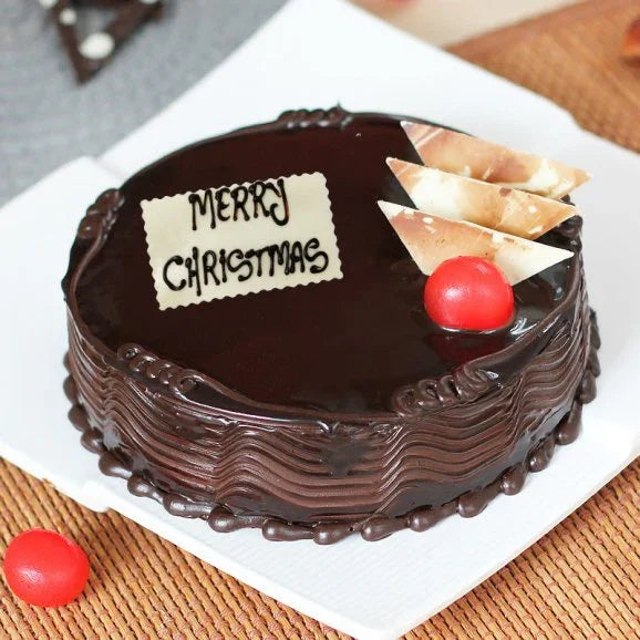 Chocolate Christmas cake with glossy icing, edible Merry Christmas plaque, red cherry, and white chocolate triangles.