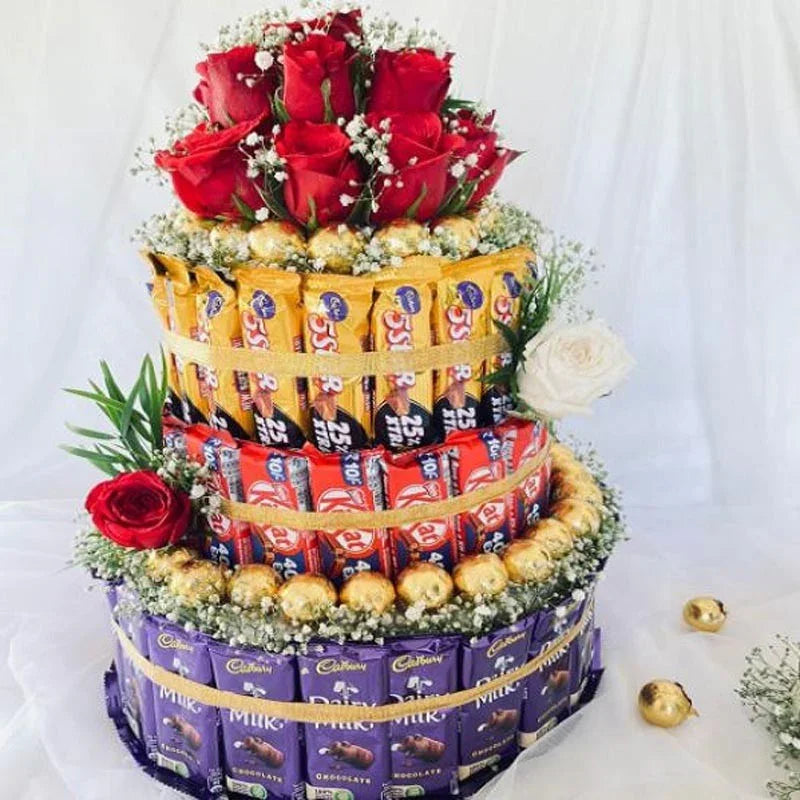 Three-tiered candy bar cake with red roses and greenery on a white background