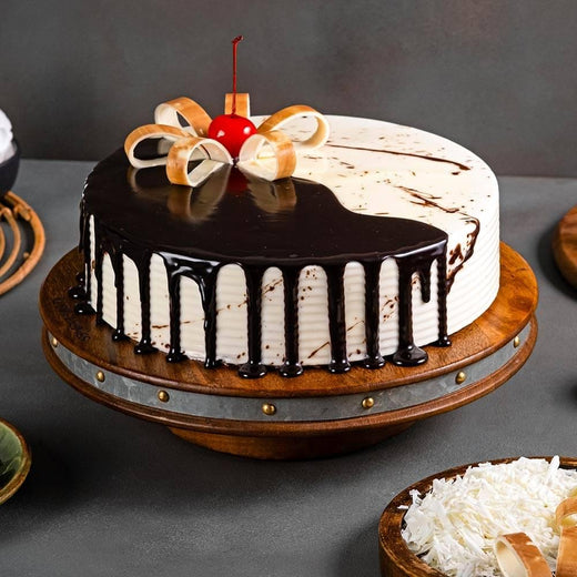 Chocolate vanilla cake with chocolate ganache drip, cherry, and white chocolate garnish on a wooden stand