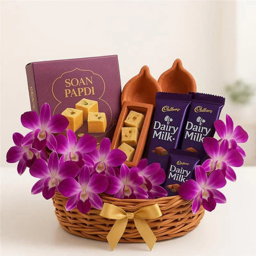 Gift basket with soan papdi, Dairy Milk chocolates, diyas, and purple orchids
