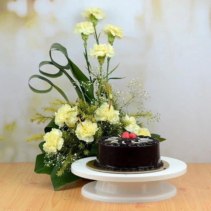 Floral arrangement with a black cake on a white stand against a light background
