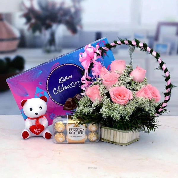 Bouquet of pink roses, Ferrero Rocher chocolates, and a Cadbury Celebration chocolate bar on a table.