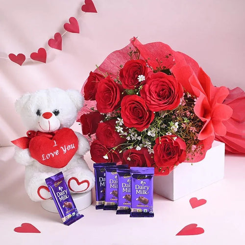 Bouquet of red roses, white teddy bear with 'Love You' heart, and Dairy Milk chocolate bars on a pink background.