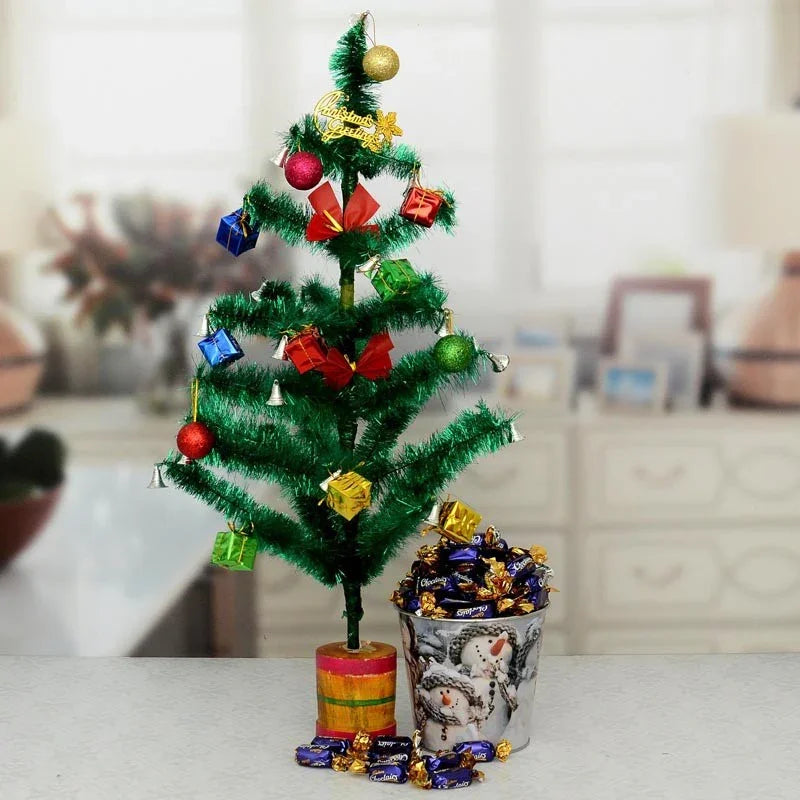 Small decorated Christmas tree with colorful ornaments in a pot on a table.