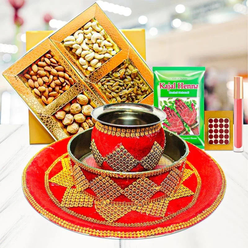Decorative cup with red and gold patterns on a white surface, surrounded by a box of nuts, Kajal Henna package, and other items.