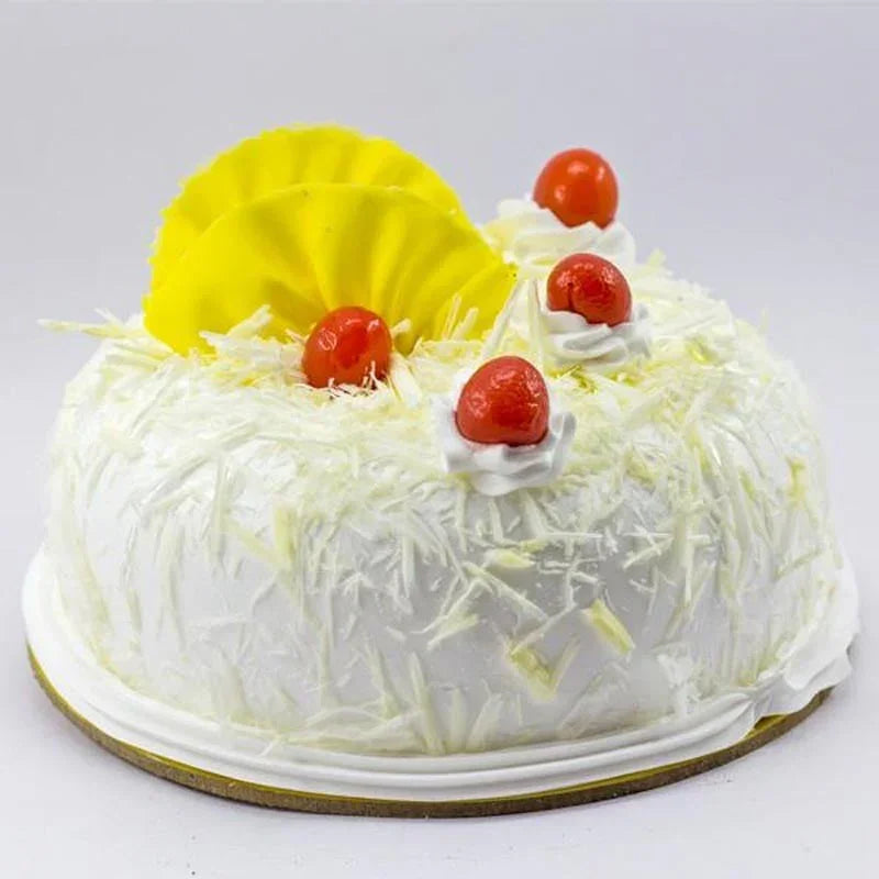 Decorative cake with white frosting, pineapple slices, and cherries on a light gray background
