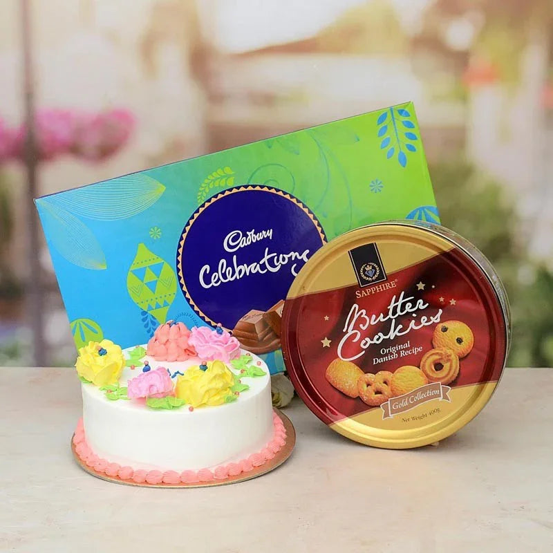 Small decorated cake with a Cadbury Celebrations box and a tin of Sapphire Butter Cookies on a blurred background.