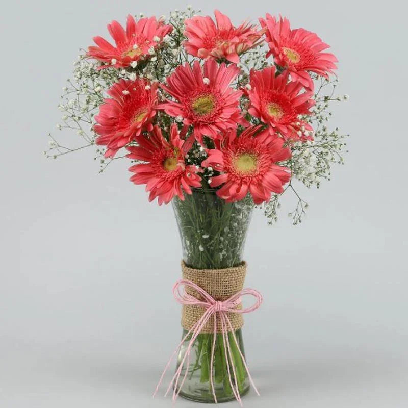 Bouquet of red flowers in a clear vase with burlap and pink ribbon on a light gray background