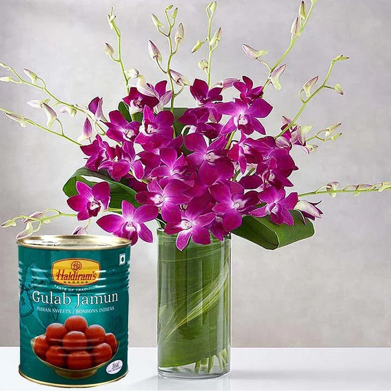 Bouquet of purple flowers in a glass vase with a can of Haldiram's Gulab Jamun on a light gray background