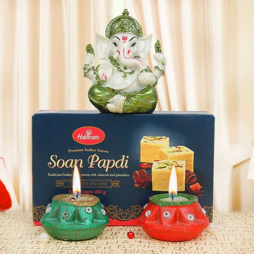 Decorative Ganesh statue of a deity on a Haldiram's Soap Papdi box with two lit candles.