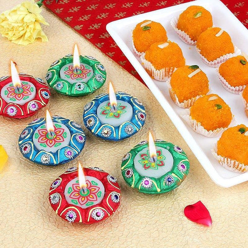 Colorful Diwali Diya with Laddu on a textured surface next to a plate of sweets.