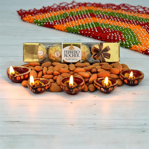 Ferrero Rocher chocolate box with almonds and lit diya candles on a wooden surface.