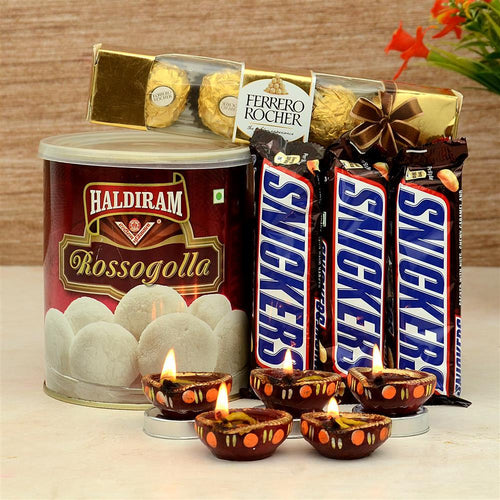 Candle holders made from Snickers and Ferrero Rocher chocolate bars next to a can of Haldiram Rossogolla on a wooden background.