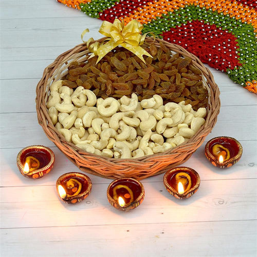 Basket of cashews and raisins with lit diya candles on a wooden surface