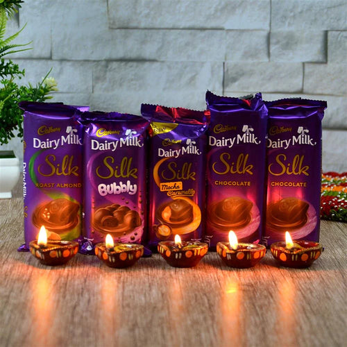Cadbury Dairy Milk Silk chocolate bars with lit candles on a wooden surface.