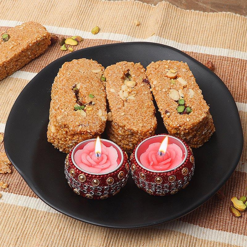 Three rectangular sweets with nuts on a black plate with two pink candles.