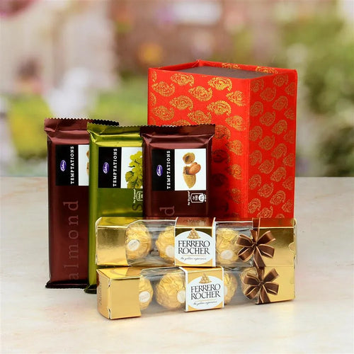 Assorted chocolate bars and Ferrero Rocher in front of a red gift box with gold patterns on a blurred background.