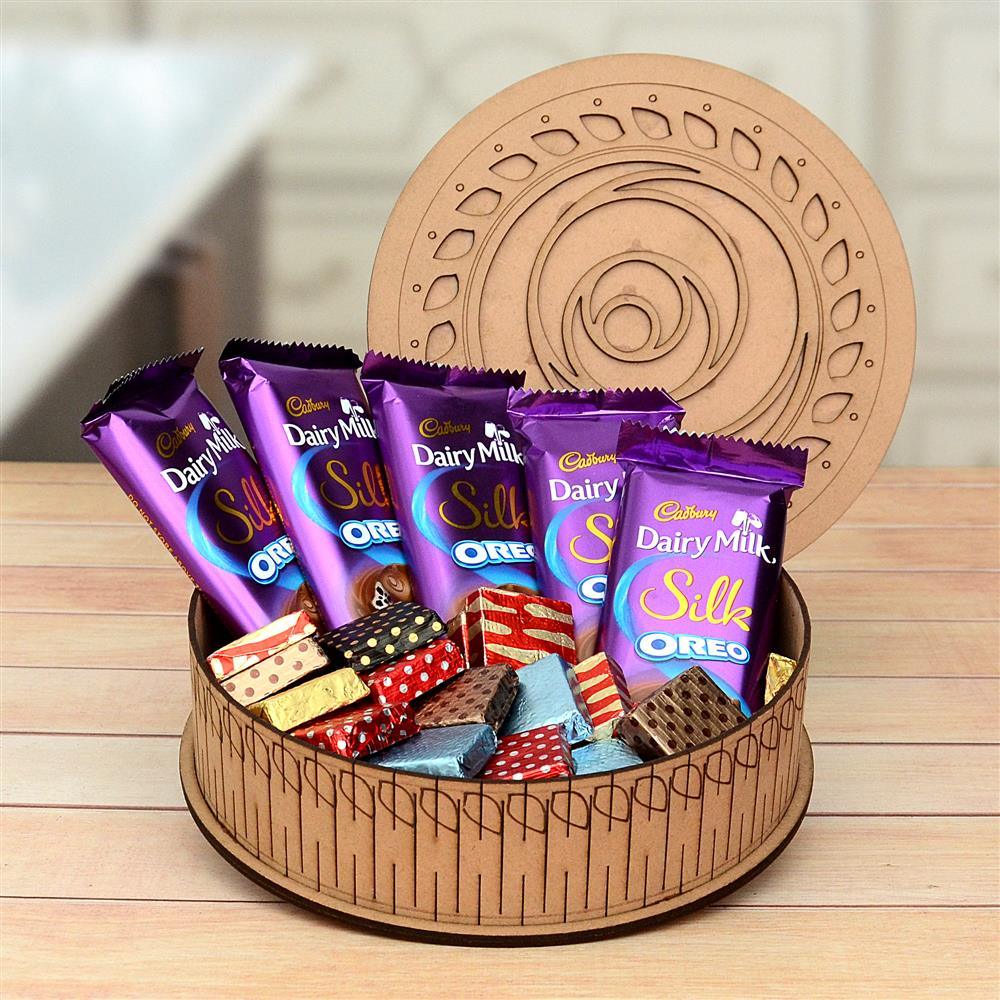 Assorted Cadbury Dairy Milk and Silk chocolate bars in a decorative wooden basket on a wooden surface.