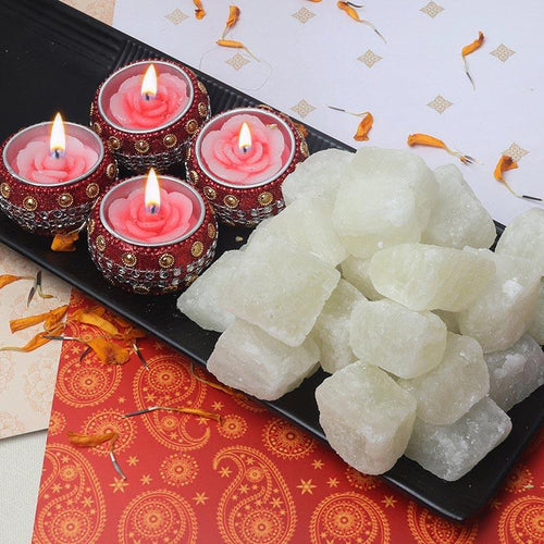 Decorative Diya with red holders and white Sweets on a black tray, placed on a patterned surface.