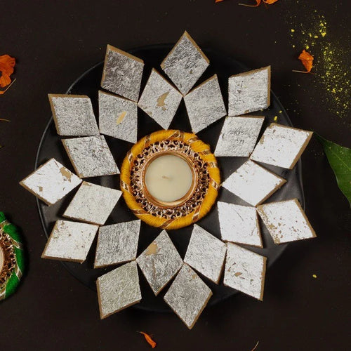 Decorative plate with kaju Katli pieces of a white dessert arranged in a circular pattern around a small candle.