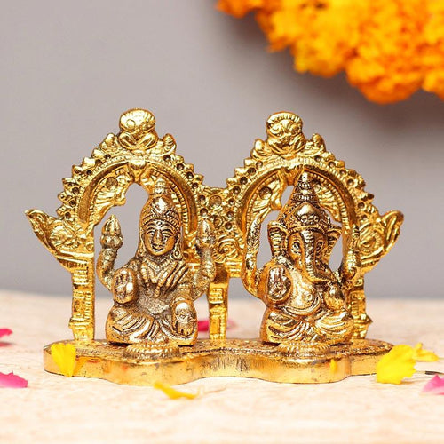 Gold-colored Laxmi Ganesh statue on a neutral background with marigold flowers.