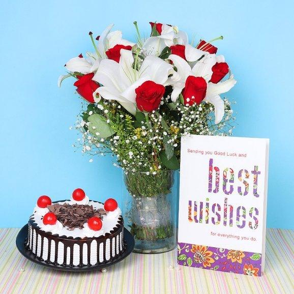 Bouquet of red and white flowers with a cake and a card on a striped tablecloth.
