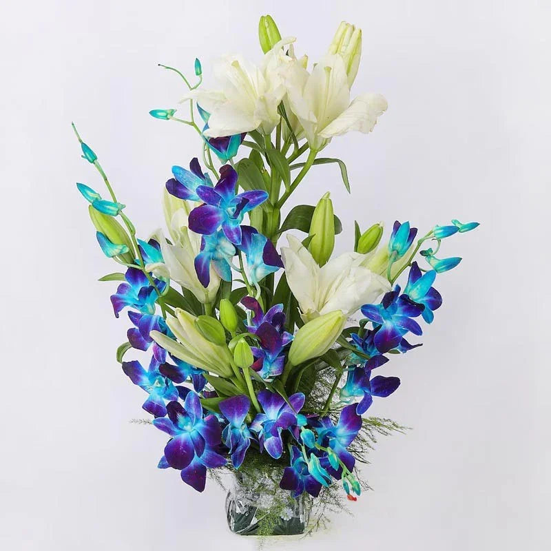 Bouquet of blue orchids and white lilies in a clear vase on a light gray background